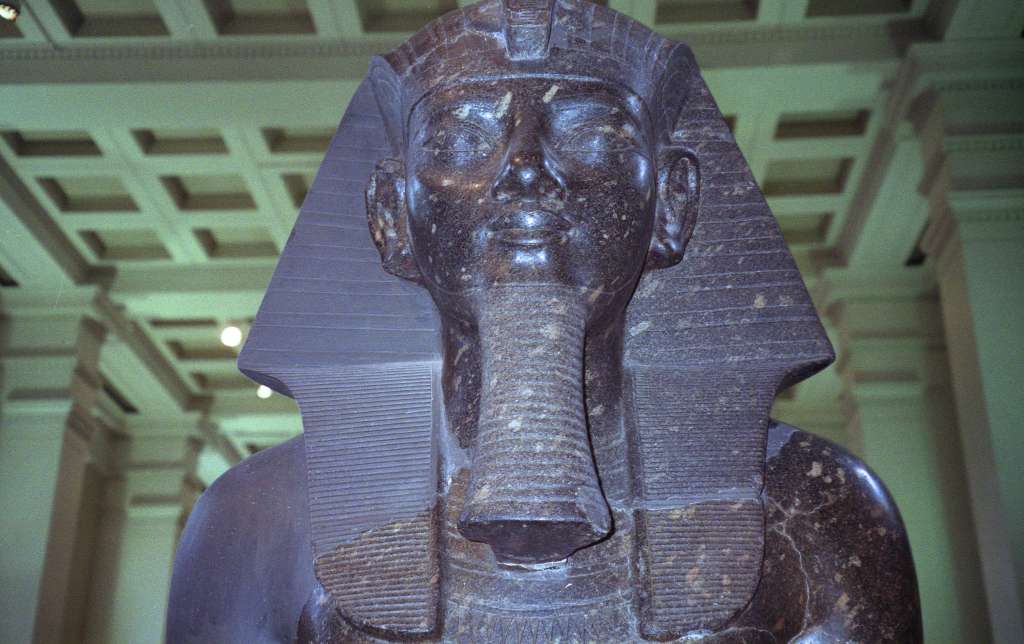 British Museum Top 20 19-2 Amenophis III Seated Statue Close Up 19. Amenophis III Seated Statue, Thebes Egypt, about 1400BC. In room 4 there are two 3m high seated statues in black granite of Amenophis III (also spelled Amenhotep). Amenhophis III was the first Egyptian King to be worshipped as a god in his own lifetime. Here is a close up of the head of the other statue, with a head-dress ornamented in front with a Uraeus, the figure of the sacred serpent that was an emblem of sovereignty.